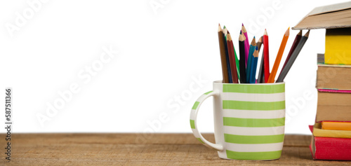 Stack of books by mug with colored pencils on wooden table