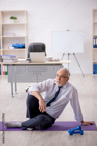 Old male employee doing sport exercises at workplace