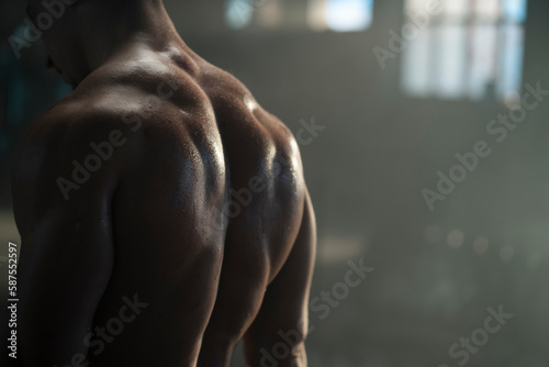 Fit muscular sweaty man with strong back muscles posing on camera at dark gym photo