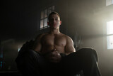 Young muscular man with six pack abs sitting on a large tyre looking at camera in gym