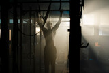 Dark view of a strong muscular man doing pull-up exercise on bar inside a abandoned warehouse against sunlight