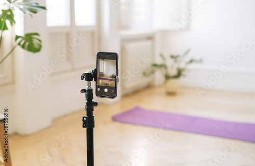 Mobile phone on tripod in empty living room with fitness mats on the floor