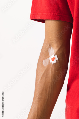 Midsection of biracial man with heart sticking plaster on arm, on white background with copy space photo