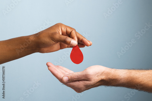 Hands of biracial man giving blood drop to caucasian man, on blue background