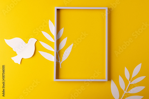 High angle view of white frame, white dove and leaves with copy space on yellow background