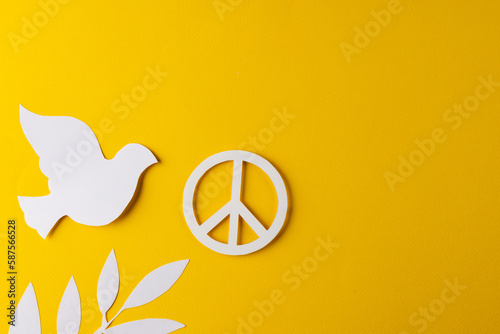 High angle view of white peace sign, white dove and leaf with copy space on yellow background