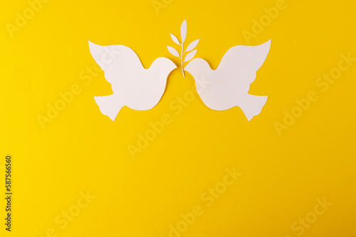 Close up of two white doves with leaf and copy space on yellow background