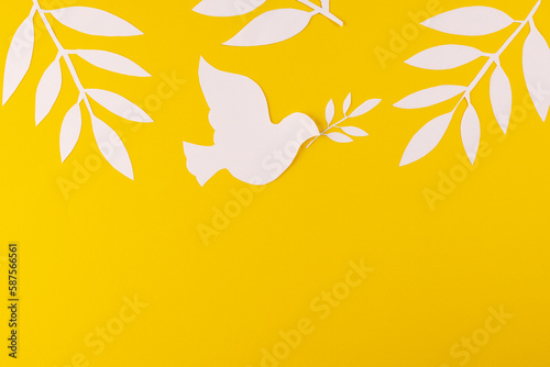 Close up of white dove with leaves and copy space on yellow background