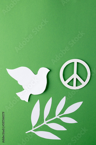 Close up of white dove and peace sign with leaves and copy space on green background