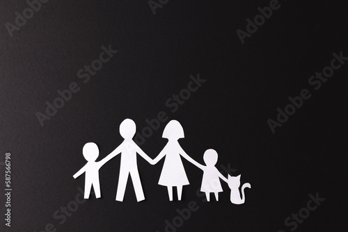 Fototapeta Naklejka Na Ścianę i Meble -  White paper cut out of family with two children and cat and copy space on black background
