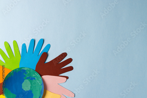 Paper cut out of multi coloured hands and globe with copy space on blue background