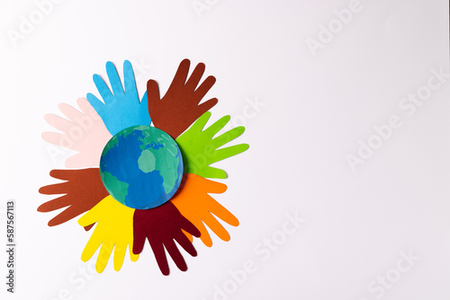 Paper cut out of multi coloured hands and globe with copy space on white background