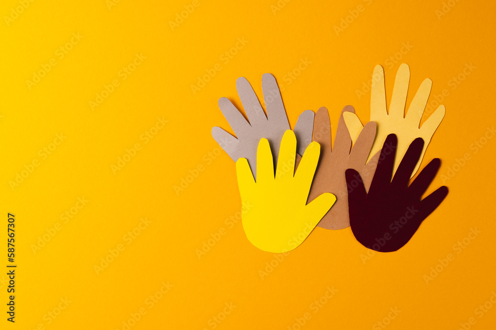 Close up of paper cut out of multi coloured hands with copy space on orange background Close up of paper cut out of multi coloured hands with copy space on orange background
