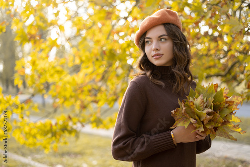 Portrait of beautiful young woman in autumn park with maple leaves in her hands. Walking outdoors in autumn.