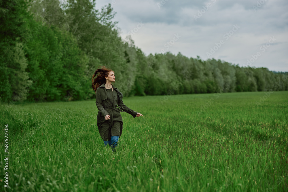 a beautiful woman in a long raincoat runs across a field in high grass in spring in cloudy weather a beautiful woman in a long raincoat runs across a field in high grass in spring in cloudy weather
