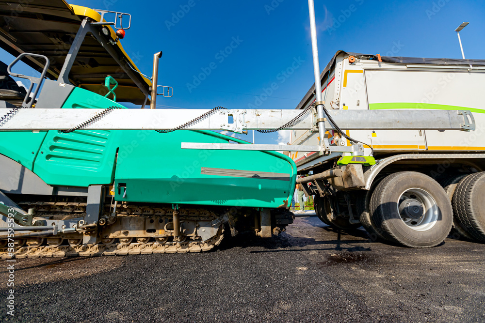 Level sensors for good road evenness placed on asphalt spreading machine, in the background truck is being prepared to loading into it