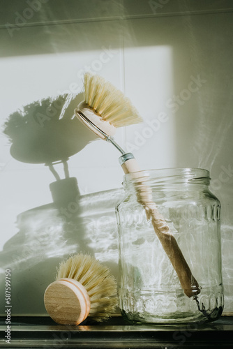 A sustainable eco dish brush is in a glass jar on a kitchen bench.