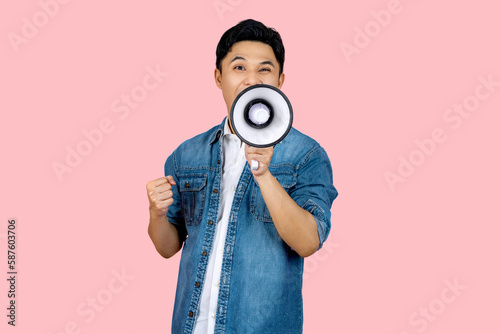Happy asian man in casual shirt t-shirt scream in megaphone shout and showing triumph gesture on workspace isolated on pink background. People lifestyle concept.