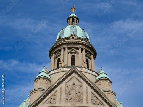 Photo of a spire with a natural frame of branches, blue sky in the background. The Christuskirche in neo-Baroque style is a Protestant church in Mannheim's Oststadt district.