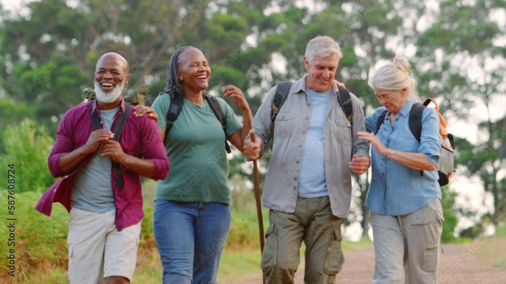 Front view shot of multi cultural group of senior friends enjoying hiking along track through countryside together - shot in slow motion