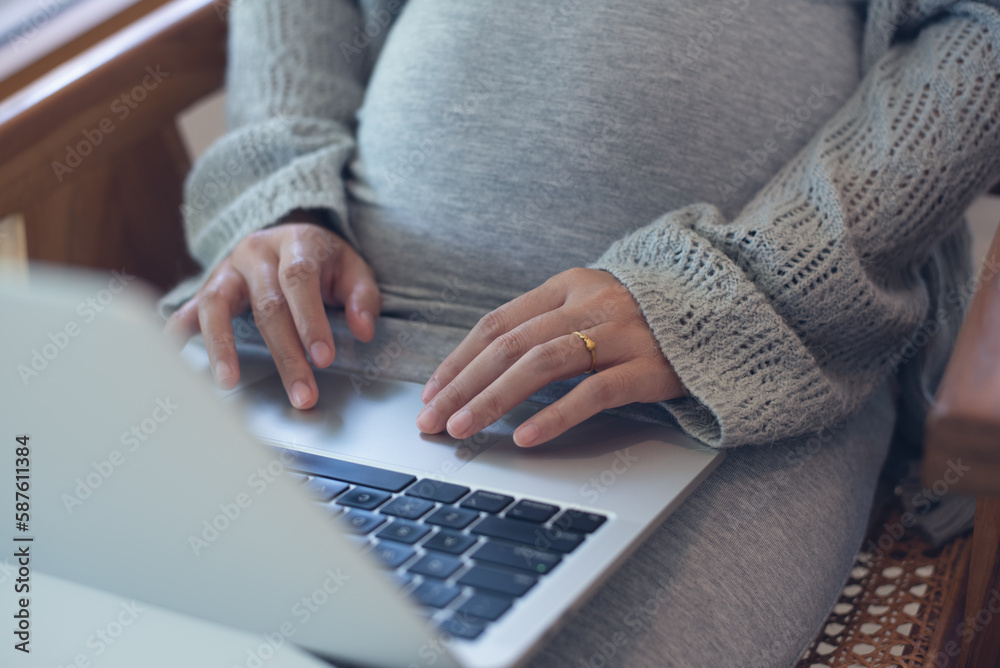 Pregnant woman working on laptop. Cropped image of pregnant businesswoman sitting at table typing on laptop at her working place in office Pregnant woman working on laptop. Cropped image of pregnant businesswoman sitting at table typing on laptop at her working place in office