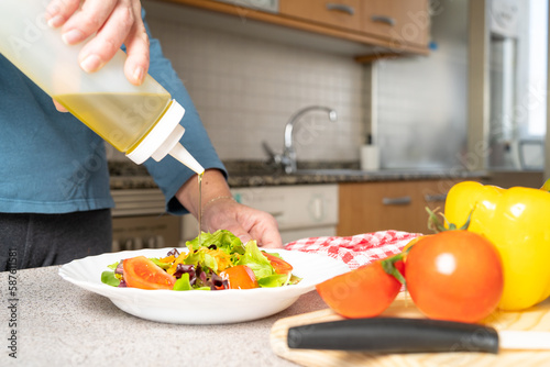 Close up of woman putting olive oil on a fresh salad of tomatoes  lettuce and carrots in the kitchen at home. Healthy and easy to make food concept. High quality photo