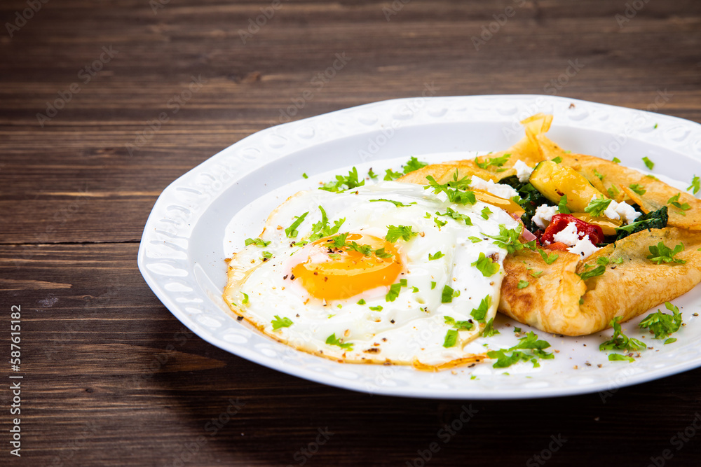 Savory crepes with feta, fried vegetables and egg on wooden background