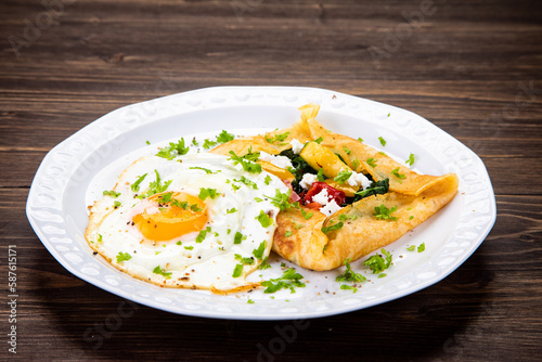 Savory crepes with feta, fried vegetables and egg on wooden background