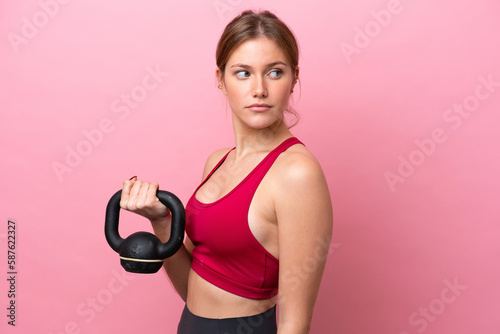 Young caucasian woman isolated on pink background making weightlifting with kettlebell © luismolinero