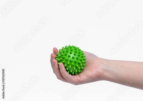 Zielona piłka z kolcami do rehabilitacji trzymana w dłoni na białym tle