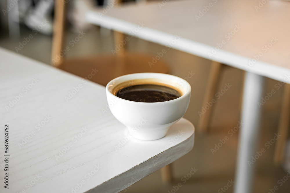 A white cup of black coffee americano on the edge of a table in a cafe
