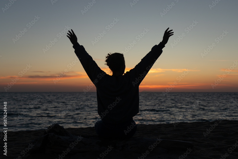 young woman backlit raising her arms in a sunset