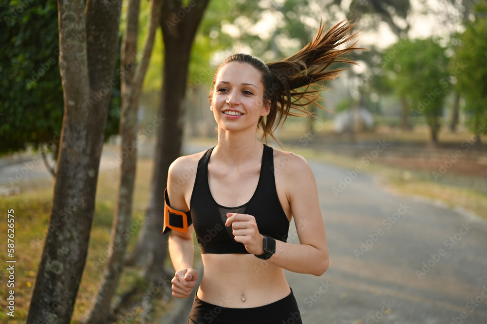 Active sporty caucasian female wearing sportswear jogging on road in summer park at sunrise. Healthy and active lifestyle concept Active sporty caucasian female wearing sportswear jogging on road in summer park at sunrise. Healthy and active lifestyle concept