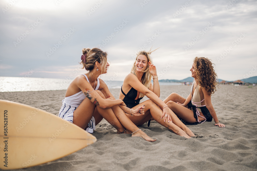 Three attractive woman friends sitting with surfboard on a beach