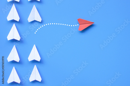 Top view of red paper airplane origami leaving other white airplanes on blue background with customizable space for text or ideas. Leadership skills concept.