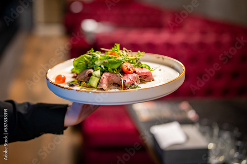 Waiter holds a plate with salad in the restaurant
