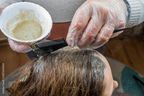 The hairdresser's hand paints gray hair roots with chemical dye using a brush. Close-up of female hair coloring. The concept of painting women's hair
