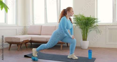 Young plump ginger fitness woman doing squat exercises with lunges from leg to leg. Fit Female is a workout at home in the living room. health and body care wellness