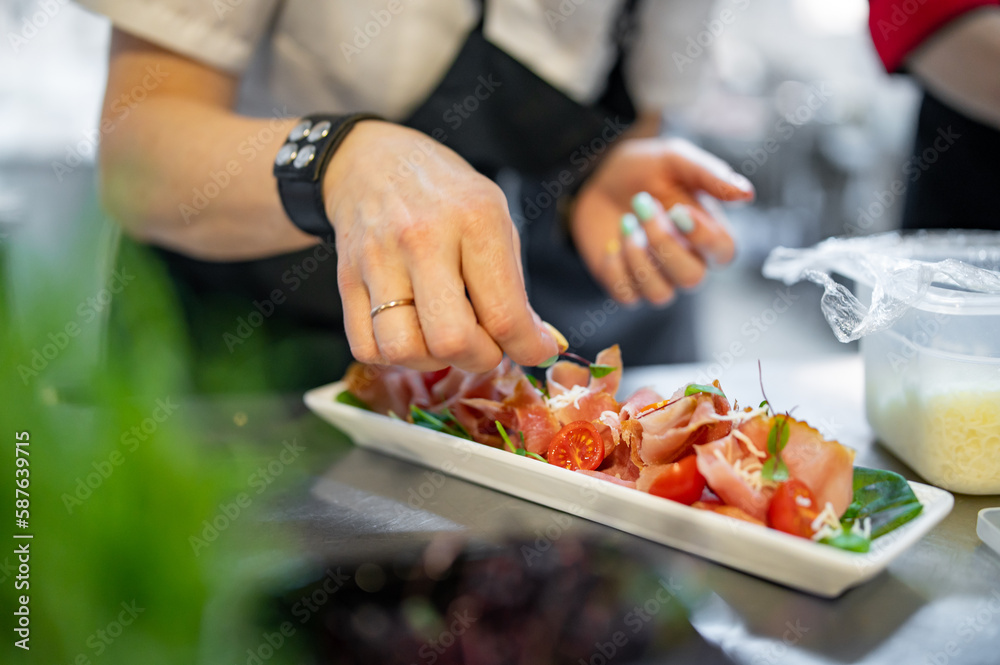 Chef decorate ready dish with slices parma ham on restaurant kitchen