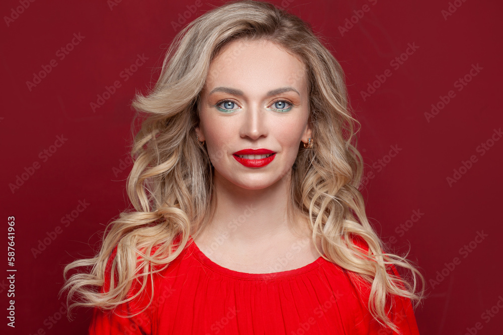 Fototapeta premium Nice woman with long curly blonde hair against red studio wall background