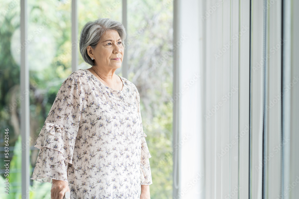 Senior Asian woman standing alone near windows in hospital. Old Asian female using walking stick at home. Retirement, health care and ageing concept Senior Asian woman standing alone near windows in hospital. Old Asian female using walking stick at home. Retirement, health care and ageing concept