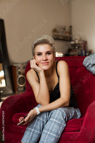 Beautiful blonde woman in black top with mobile phone in hand sitting on red sofa