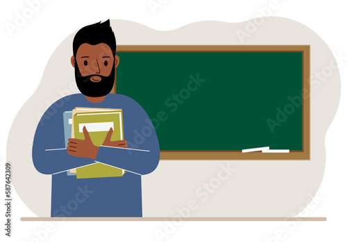Male teacher with books on the background of the school board.
