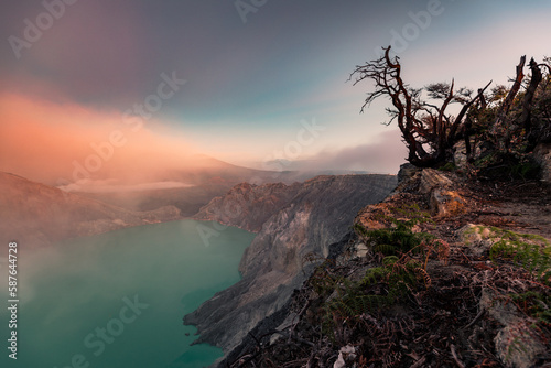 Sunrise over Kawah Ijen Volcano revealing acid turquoise lake and toxic sulfur gases and dead trees next to illegal mining operation, Java, Indonesia photo