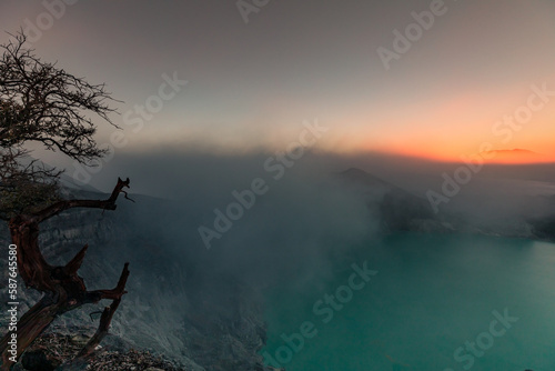 Sunrise over Kawah Ijen Volcano revealing acid turquoise lake and toxic sulfur gases and dead trees next to illegal mining operation, Java, Indonesia photo