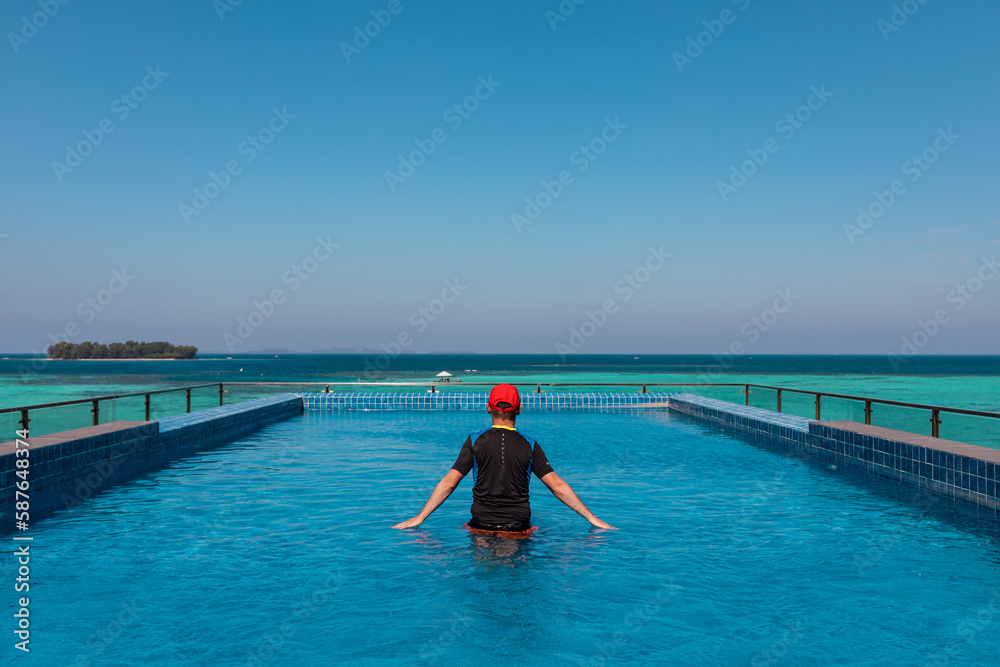 Fototapeta premium Man relaxing in the infinity pool hanging over turquoise lagoon of Karimunjava Indonesian tropical island. 