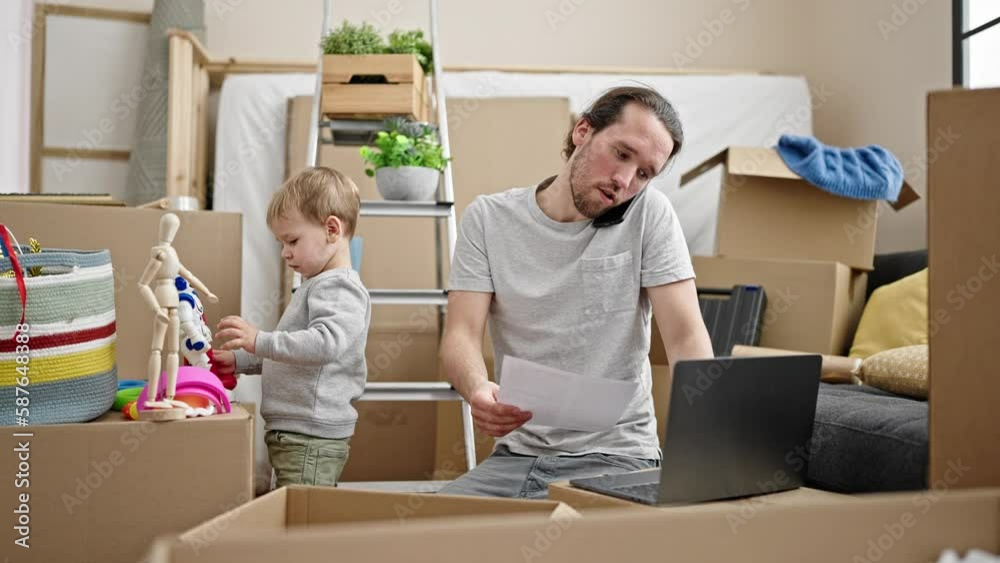 Father and son unpacking cardboard box using laptop talking on smartphone at new home Father and son unpacking cardboard box using laptop talking on smartphone at new home