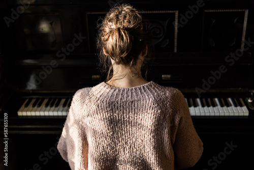 woman playing piano, back view, old rustic black instrument