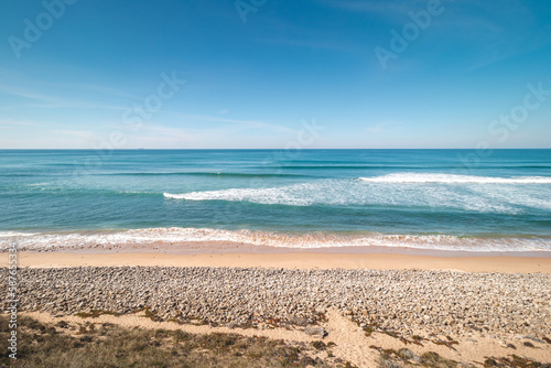 Fototapeta Naklejka Na Ścianę i Meble -  Atlantic Ocean, with its waves, has washed up on the Portuguese coast a multitude of pebbles on the sandy beach, creating a beautiful setting for a day out. Fisherman Trail