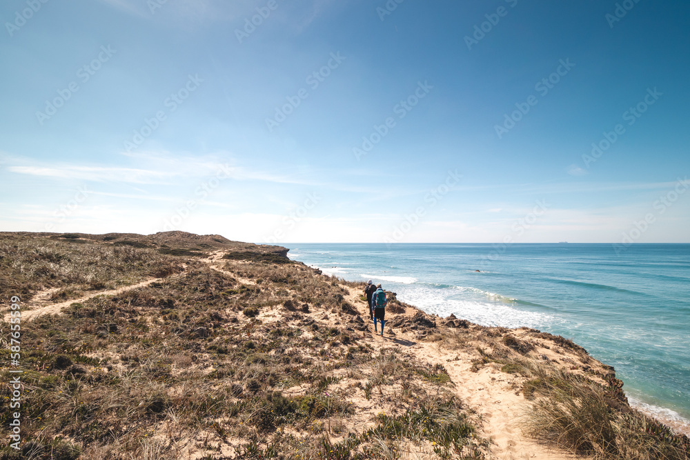 Passionate adventurers walk the rugged, dry coastline with cliffs around the Atlantic Ocean on a trail called the Fisherman Trail in Portugal